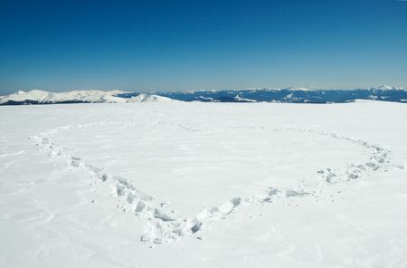 Human footprint form the heart shape on snow-covered mountainside plateau and mountain ranges behindの写真素材