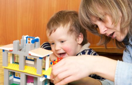 Mother with small son play with building set for children (built a house)