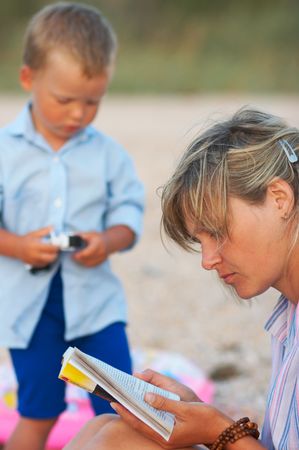 mother read book on evening sandy coast and small boy nearの写真素材