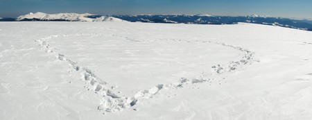 Human footprint form the heart shape on snow-covered mountainside plateau and mountain ranges behind. Five shots stitch image.の写真素材