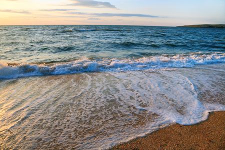 Sea surf wave break on sunset sandy coastline