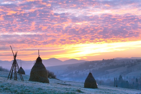 first autumn frosts on pasture with haystacks and majestic sunrise in the mountains villageの写真素材