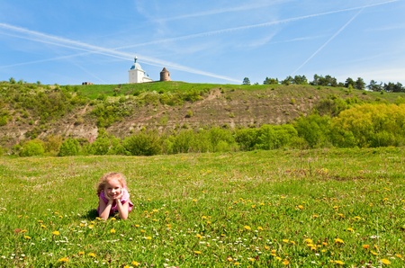Small happy girl on spring blossoming field and ancient fotess and church behind