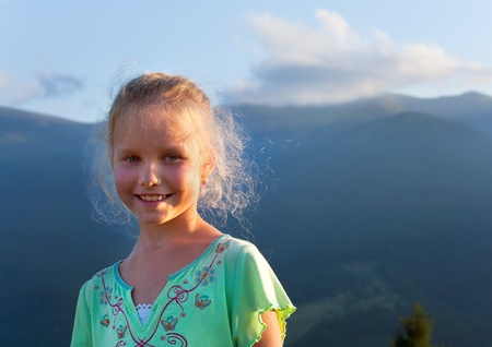 Small girl outdoor portrait in last sunset sunlight and summer mountain behindの写真素材