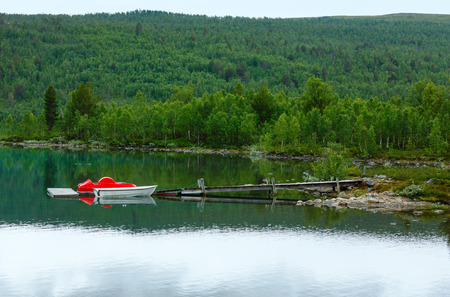 Summer cloudy Otta fjord coast landscape with boad near coast (Norway).