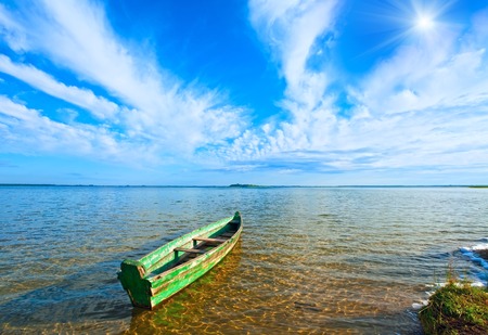 Old wooden fishing boat on summer lake bank and sunshine in blue sky (Svityaz, Ukraine)の写真素材