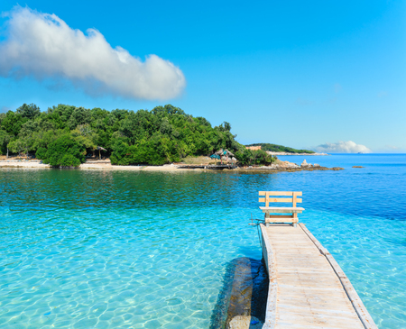 Beautiful Ionian Sea with clear turquoise water, wooden pier and morning summer coast view from beach (Ksamil, Albania).の写真素材