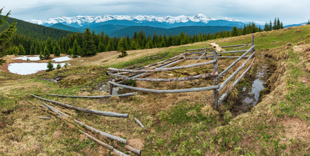 Spring Carpathian mountains landscape with snow-covered tops of Chornohora ridge in far, Ukraine.  Fenced farming area with water spring and drinker.の写真素材