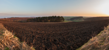 Spring early morning rural country landscape with plowed agricultural fields on hills, groves  and village outskirts in far. Arable and growth farmlands in tender delicate daybreak sunlight.の写真素材