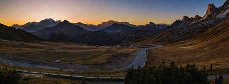 Sun glow in evening hazy sky. Italian Dolomites mountain silhouettes panoramic peaceful view from Giau Pass. Climate, environment and travel concept scene. Cars unrecognizable.の写真素材