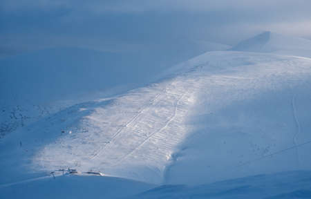 Snow covered mountain slope in last evening sunlight. Magnificent windy dusk on picturesque alpine...