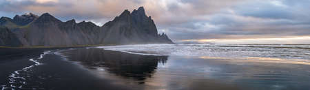 Sunrise Stokksnes cape sea beach and Vestrahorn Mountain with its reflection on wet black volcanic sand surface, Iceland. Amazing nature scenery, popular travel destination.の写真素材