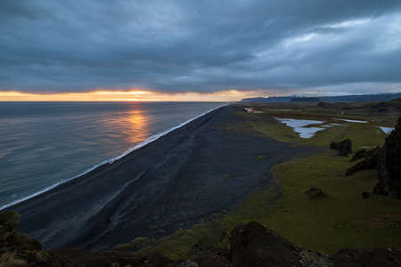 Picturesque autumn evening view to endless ocean  black volcanic sand beach from Dyrholaey Cape, Vik, South Iceland. Vestmannaeyjar islands weird silhouettes on horizont.の写真素材