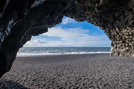 View to Reynisfjara ocean Black Sand Beach from cave at the foot of the Reynisfjall mount.Basalt rock pillars columns. Vik, South Iceland. Unique geological volcanic formations.の写真素材