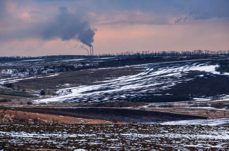 Calm evening sunset in the Ukrainian countryside. Arable land covered with the last snow, early spring Industrial chimneys of Burshtyn TPP on the horizon.の写真素材