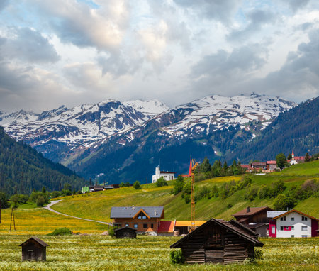 Summer Alpine mountain country view with grassy meadow and road to village (Austria)の写真素材