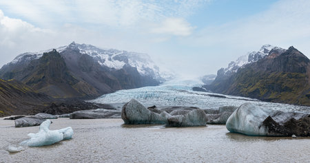 Glacier tongue slides from the Vatnajokull icecap or Vatna Glacier near subglacial Oraefajokull volcano, Iceland. Glacial lagoon with ice blocks and surrounding mountains.の写真素材