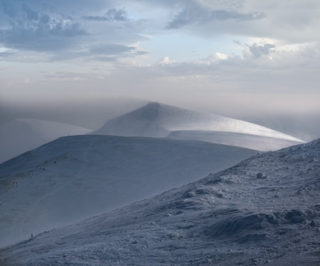 Snow covered mountain slope in last evening sunlight. Magnificent windy dusk on picturesque alpine ski resort, Dragobrat, Ukraine, Carpathian Mountains.の写真素材