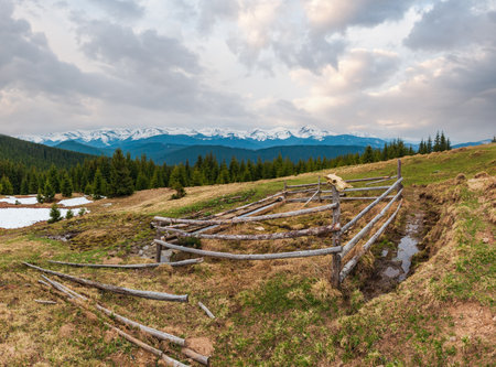 Spring Carpathian mountains landscape with snow-covered tops of Chornohora ridge in far, Ukraine.  Fenced farming area with water spring and drinker.の写真素材
