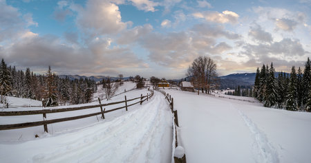 Secondary countryside alpine road in remote mountain village, snow drifts and wood fence on waysideの写真素材