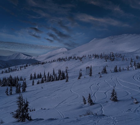 Alpine resort ski lift with seats going over the pre sunrise night mountain skiing freeride slopes and fir tree groves. Svydovets ridge view from Dragobrat ski resort.の写真素材