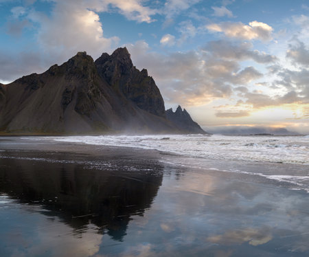 Sunrise Stokksnes cape sea beach and Vestrahorn Mountain with its reflection on wet black volcanic sand surface, Iceland. Amazing nature scenery, popular travel destination.の写真素材