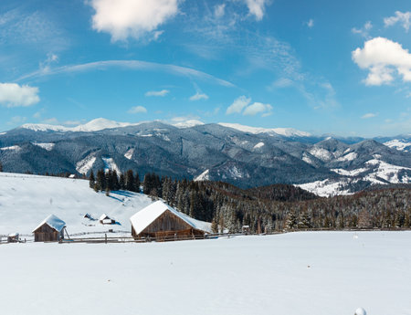 Picturesque snowy winter Skupova mountain slope and lone farmhouse on plateau farmstead, Carpathian, Ukraine, Verkhovyna district. Chornohora ridge and Pip Ivan with observatory in clouds behind.の写真素材