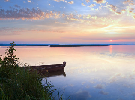 Sunset and old wooden fishing boat near the summer lake shore (Svityaz, Ukraine)の写真素材