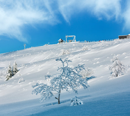 Morning winter calm mountain landscape with beautiful frosting trees, snowdrifts on slope and ski lifts in far (Carpathian Mountains, Ukraine). Skiers are unrecognizable.の写真素材