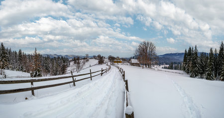 Secondary countryside alpine road in remote mountain village, snow drifts and wood fence on waysideの写真素材