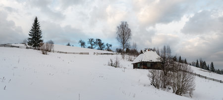 Countryside hills, groves and farmlands in winter remote alpine mountain village, and small old abandoned house on hillsideの写真素材