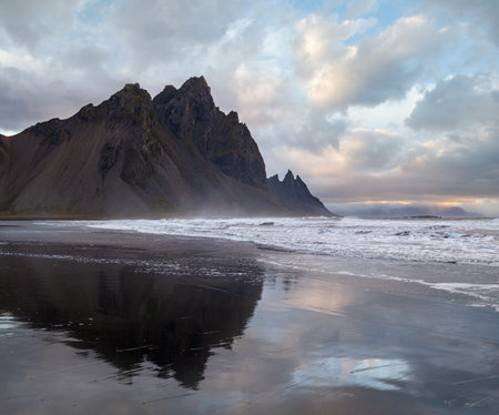 Sunrise Stokksnes cape sea beach and Vestrahorn Mountain with its reflection on wet black volcanic sand surface, Iceland. Amazing nature scenery, popular travel destination.の写真素材