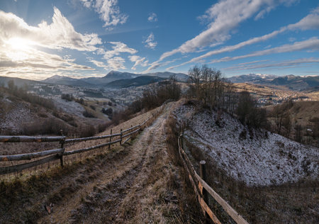Winter coming. Last good weather days in autumn mountain countryside morning picturesque scene. Dirty road from hills to the village. Hoverla and Petros Ukrainian Carpathians mountains in far.の写真素材