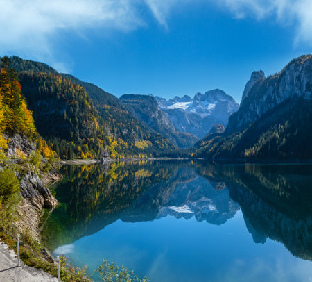 Sunny idyllic colorful autumn alpine view. Peaceful mountain lake with clear transparent water and reflections. Gosauseen or Vorderer Gosausee lake, Upper Austria. Dachstein summit and glacier in far.の写真素材