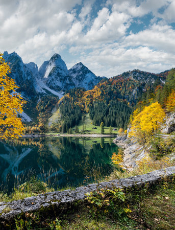 Sunny idyllic colorful autumn alpine view. Peaceful mountain lake with clear transparent water and reflections. Gosauseen or Vorderer Gosausee lake, Upper Austria. Dachstein summit and glacier in far.の写真素材