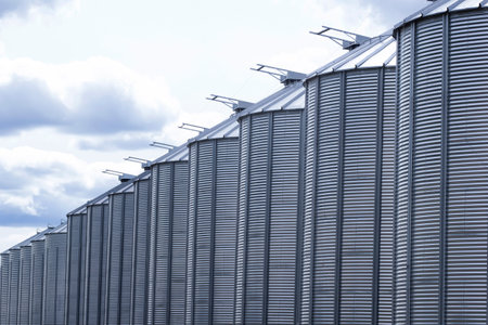 Row of stainless steel gray grain bins and cloudy sky in prairies.