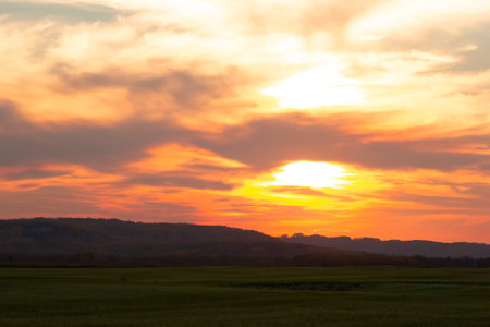 Feather clouds above the prairies and hills in the orange sunset time. Sun is behind clouds.の写真素材
