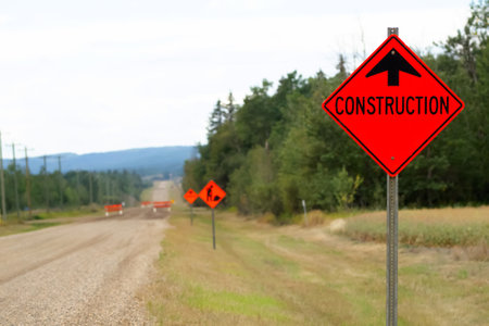 Road closed and bright orange construction sign in the country road through the forest without pavement.の写真素材