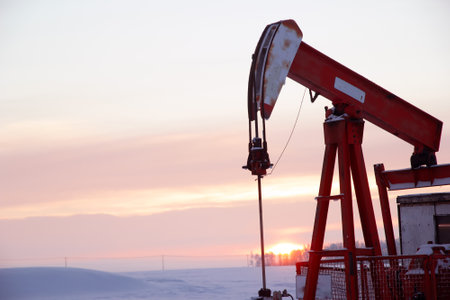 One red pump jack in the agricultural field covered with snow in winter in the sunset time.の写真素材