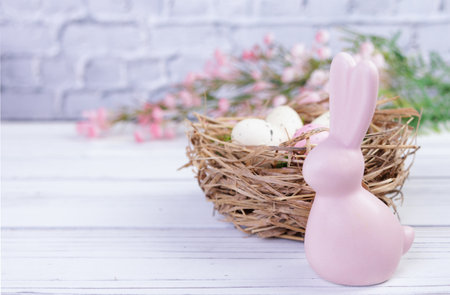 Easter banner composition with flowers, nest with speckled eggs and moss on the white wooden background, pink bunny figurine, top view.の写真素材