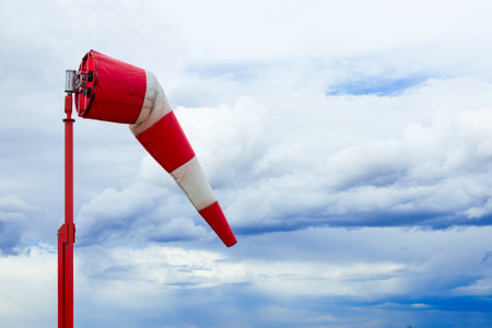 Striped red and white weather vane in wind with dark blue cloudy sky.の写真素材