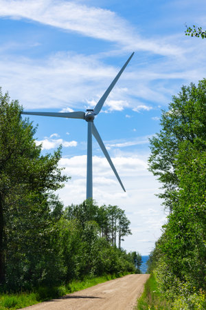 Wind turbine is producing green energy in the rural area among trees and near the country road in...