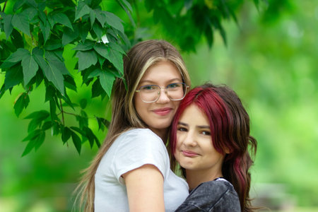 Two teenage girls (one with red dyed hair) are hugging in the park, real people, cheerful and happy...
