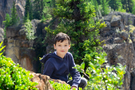 Active healthy teenage Caucasian boy in blue hoodie climbed on mountain cliff with trees and creeper plants. Sulphur gates, Grande Cache, Alberta, Canada.の写真素材