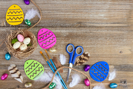 Vibrant Easter craft composition on the brown rustic wooden table with colored wooden eggs, paint brushes, scissors, candies, jute twine and nest with speckled eggs and feathers.の写真素材