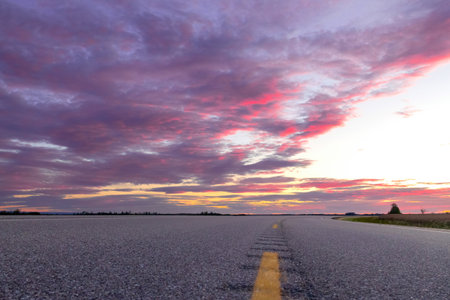 Spectacular purple and pink sunset in prairies with cloudy sky over the highway through the...