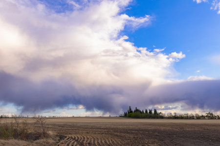 A scenic rural landscape capturing a freshly seeded agricultural field under a dramatic cloudy spring sky, raining in the horizon.の写真素材