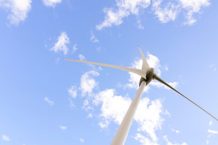 Blades of the windmill generating electricity on the background of blue cloudy sky, source renewable...