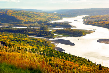 View from the hill to the river down in the valley surrounded with forests with yellow and green...