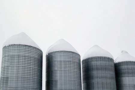 Agricultural steel grain bins storing seeds in cold frosty winter. Snowbanks in the farm and on...